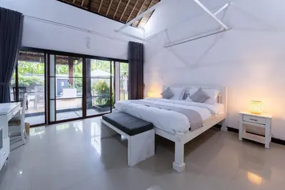 a white bedroom with a bed and a large window at Karen's Tropical Villa in Seminyak