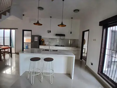 a kitchen with a white island with two bar stools at Villa Rumah Lemon Nusa Dua in Nusa Dua