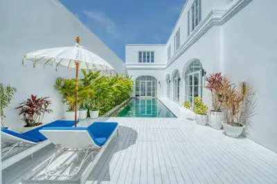 a house with a swimming pool and two chairs and an umbrella at Colonial Style 3BR Walking Distance to the Beach in Canggu