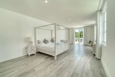 a white bedroom with a bed with a large mirror at Colonial Style 3BR Walking Distance to the Beach in Canggu