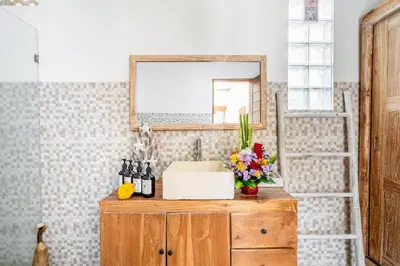 a bathroom sink with a mirror and flowers on a wooden dresser at Villa Avaluna by JB Villas in Seminyak