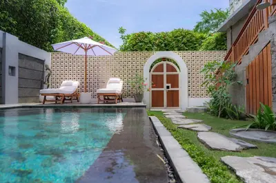 a swimming pool with two chairs and an umbrella at Kania Rooms & Suite in Seminyak