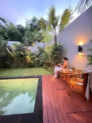 a woman sitting on a table next to a pool at Villa in South Kuta Dewi Amerta villa in Jimbaran