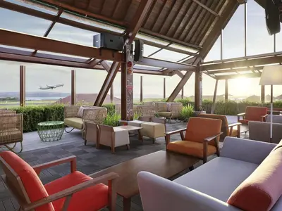 a patio with chairs and tables and an airplane in the sky at Novotel Bali Ngurah Rai Airport in Kuta