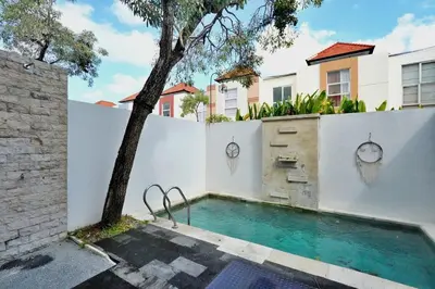 a swimming pool with a tree next to a white fence at NR Villa, 2 Bedroom Villa Kerobokan in Seminyak
