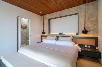 two beds in a bedroom with a stone wall at Modern 3BR Villa Seminyak, central location in Seminyak