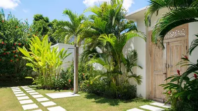 a garden with palm trees and a wooden door at Alea Estate by Villa Finder in Kerobokan