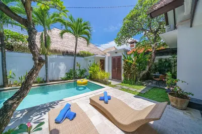 a backyard with a swimming pool with two chairs and a tree at Villa Sun Seminyak in Seminyak