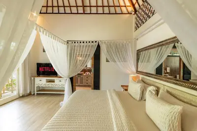 a bedroom with a large bed with white curtains at Luxury Aliya Villa by Betterplace in Sanur