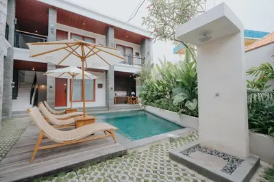 a villa with a swimming pool and two chairs and an umbrella at Casa Nika Suites Seminyak in Seminyak