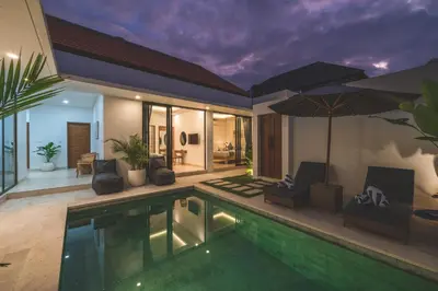 a villa with a swimming pool with chairs and an umbrella at Villa Kusuma 3 Seminyak in Badung