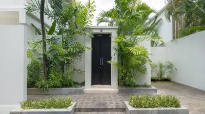 a white house with a black door and palm trees at Villa Merta Sari 10 by Villa Finder in Seminyak