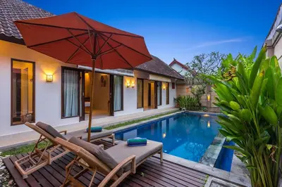 a patio with chairs and an umbrella next to a swimming pool at Villa Alamanda, central location and close to restaurants in Seminyak
