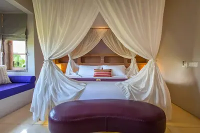 a bedroom with a canopy bed with a purple couch at Kevia Peaceful 3 BR Private Pool Villa in Seminyak