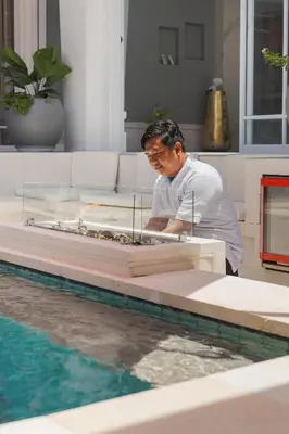 a man standing next to a table next to a pool at Xxtra Villa in Seminyak