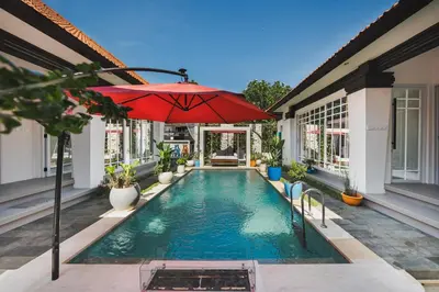 a swimming pool with a red umbrella and a house at Xxtra Villa in Seminyak