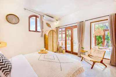 a bedroom with a bed and a chair and windows at 3BR Villa | Seminyak Central | 450m From Beach in Seminyak