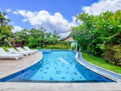 a swimming pool with white lounge chairs next to a villa at Harmony Beach Suite in Seminyak