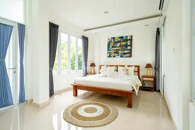 a white bedroom with a bed and a large window at Mertasari Beach Villa Sanur - 3 BR in Sanur