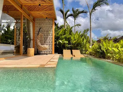 a swimming pool with chairs and a house with palm trees at Desa Hut - Serene Tropical Hideaway Rice Fields near Seminyak in Kerobokan