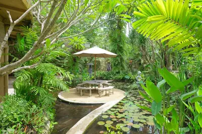a patio with a table and an umbrella in a garden at Mosaic Villa Sanur in Sanur