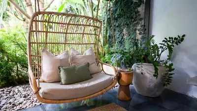 a rattan chair with pillows on a patio at Villa Honeypot Berawa in Canggu