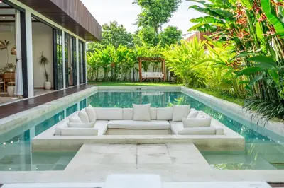 a poolside living room with white furniture next to a house at Palm Sugar 2-Chic 3BR Villa in Jimbaran with Pool&Garden in Jimbaran