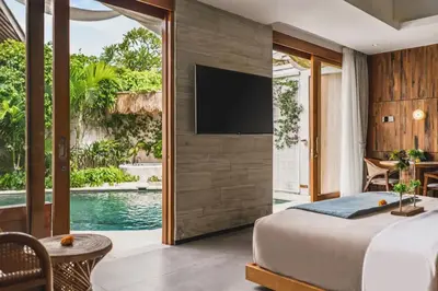 a bedroom with a tv on a wall next to a pool at Charity Stunning Grand 1 BR Pool Villa With Jacuzzi in Seminyak
