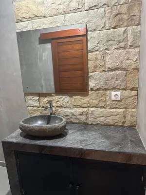 a bathroom sink with a mirror and a stone wall at Villa Inges 3 Seminyak in Seminyak