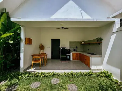 an open kitchen with a table and a refrigerator at Soane Summer House by AGATA in Seminyak