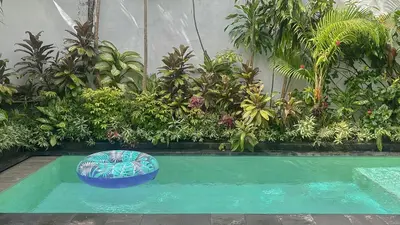 a swimming pool with a seat in front of plants at New 2BR Mahaprada Private Pool in Seminyak in Seminyak