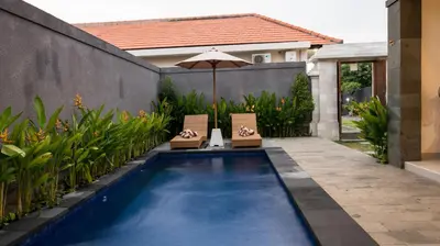 a swimming pool with two chairs and an umbrella at Villa Inges 1 Seminyak in Seminyak