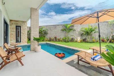 a patio with a pool and chairs and an umbrella at Villa nia gray 1 in Seminyak