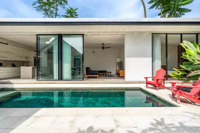 a pool in the backyard of a house with glass walls at Villa Semilir Pagi, Canggu in Canggu