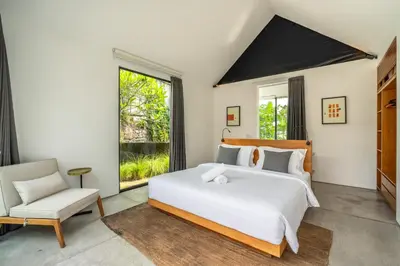 a bedroom with a large white bed and a chair at Villa Semilir Pagi, Canggu in Canggu