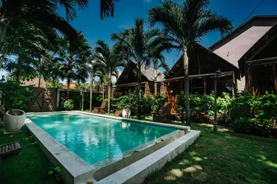 a swimming pool in front of a house with palm trees at Wow Cozy Lagoon! in Nusa Dua