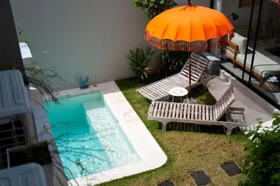 an umbrella and chairs next to a swimming pool at Charming 3 BR villa in the heart of Umalas in Canggu