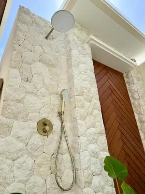 a bathroom with a shower in a stone wall at House of Rakiki Legian - 2BR Private Pool Villa in Central Legian close to Beach in Legian