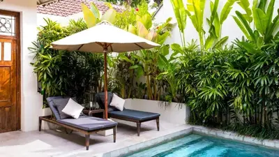 a patio with two chairs and an umbrella next to a swimming pool at Seminyak Pool Villa in Seminyak