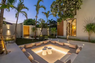 a patio with a couch and a table and palm trees at Villa Batu, Superb 4BR beachside in Canggu