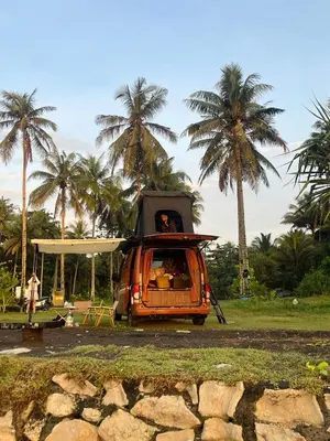 an orange van parked in a field with palm trees at Wandervan - Bali Campervan Rental in Kuta