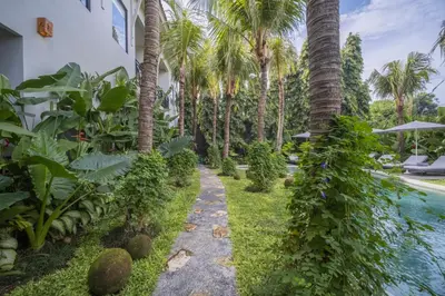 a garden with palm trees and a swimming pool at Anam Mani New Room Central Seminyak in Seminyak