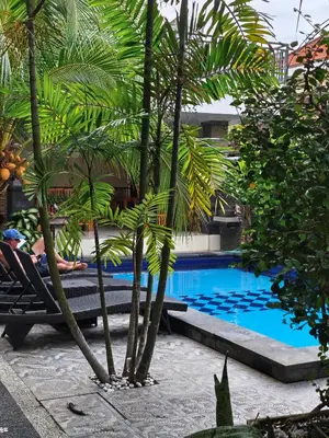 a person sitting in a chair next to a pool with palm trees at Jepun segara homestay in Ngurah Rai International Airport