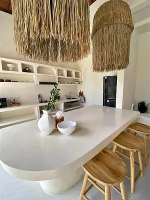 a kitchen with a large white counter with chairs and chandeliers at Villa Makna Canggu in Canggu