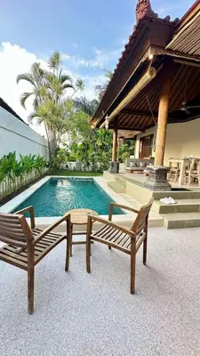 a swimming pool with two benches next to a house at Authentic Balinese Riverside Villa in Kerobokan