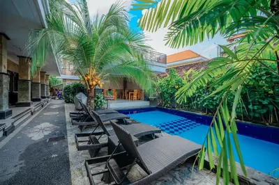 a resort pool with chaise lounge chairs and palm trees at Wana Kubu Suite and Dormitory in Ngurah Rai International Airport