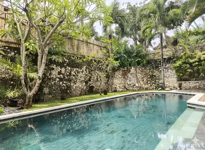 a swimming pool in front of a stone wall at Calladi Villa in Seminyak