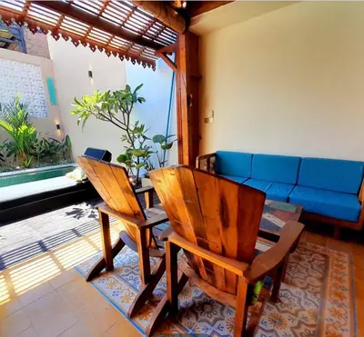 a living room with two wooden chairs and a blue couch at Joglo Raera Bali in Seminyak