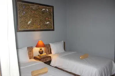 two beds in a room with a picture on the wall at Samblung Mas House in Denpasar