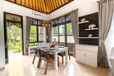 a dining room with a table and chairs and windows at D'Maya Villa Jimbaran By Island Escape in Jimbaran